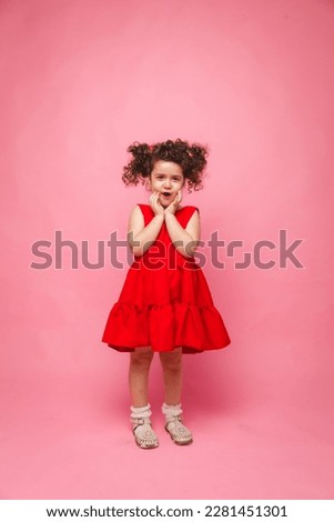 emotional portrait of a little girl in a red dress on a pink background.