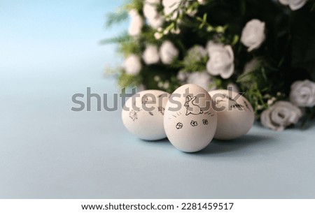 White chicken painted eggs on a blue background and with a bouquet of flowers. Three Easter eggs with a bunny on them. Close up. Free copy space.