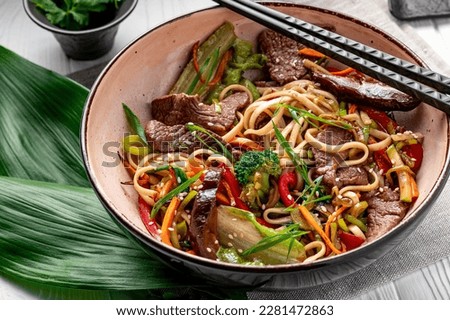 Udon stir fry noodles with beef meat and vegetables in a plate on white wooden background. Asian cuisine. Delicious and healthy food. Photo for the menu. Royalty-Free Stock Photo #2281472863