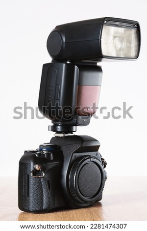 Black photographic camera without lens and with handheld flash on top, on wooden table and white background, photography theme, visual communication, right side view Royalty-Free Stock Photo #2281474307