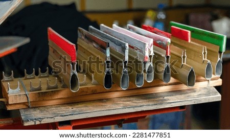 silk screen production. serigraphy printmaking. squeegees isometric projection on wooden shelve of the print screening apparatus. printing images on t-shirts by silk screen method in a design studio Royalty-Free Stock Photo #2281477851
