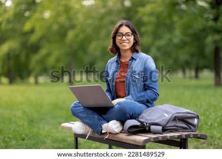 Smiling Arab Female Student In Eyeglasses Using Laptop Outdoors, Happy Young Middle Eastern Woman Sitting On Bench Outside And Study Online On Computer, Enjoying Remote Education Royalty-Free Stock Photo #2281489529