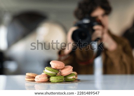 Young man with professional camera taking food photo in photostudio, photographer working and taking pictures of macarons, selective focus on sweets
