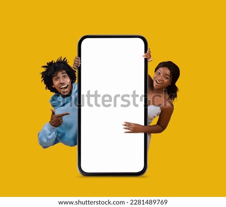Excited Young Black Man And Woman Pointing At Big Blank Smartphone Isolated Over Yellow Background, Cheerful African American Couple Recommending New Mobile Offer Or Website, Collage, Mockup