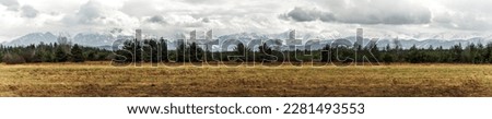 Panoramic view on Tatra Mountains, Poland seen from further. Snow-covered peaks of the rocky mountains and cloudy sky in the time of early spring. Natural background.