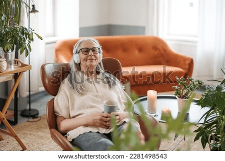 Senior woman resting with cup of tea in her living room, listening music. Royalty-Free Stock Photo #2281498543