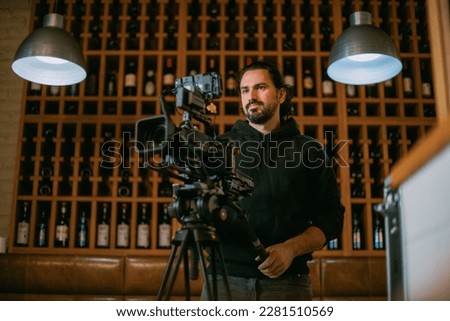 Director of photography with a camera in his hands on the set. Professional videographer at work on filming a movie, commercial or TV series. Filming process indoors, studio Royalty-Free Stock Photo #2281510569