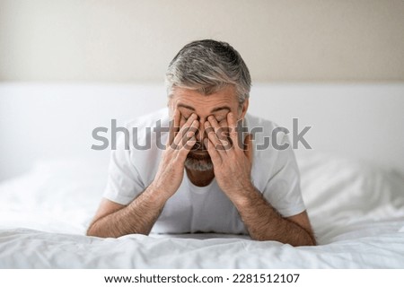 Sleeping disorder. Closeup of exhausted grey-haired middle aged man lying in bed in the morning, rubbing eyes, feeling tired after sleepless night, white bedroom interior, copy space Royalty-Free Stock Photo #2281512107