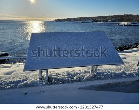 An information sign along the water that is covered in snow.