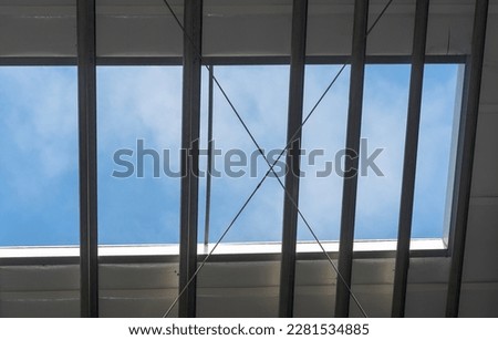 Roof window in an industrial hall. Blue sky with clouds, visible through the window "frame" like a picture. Production hall - roof skylight (ventilator).  