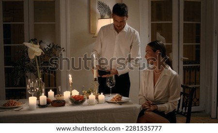 Positive couple celebrating date at night apartment closeup. Gentle man filling wine glass for wife. Happy family enjoying alcohol on evening anniversary. Tender lovers having romantic dinner at home