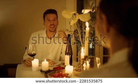 Positive man speaking at candles table room closeup. Unknown woman silhouette listening boyfriend at night place. Young newlyweds having romantic date. Enamoured lovers dining together at evening Royalty-Free Stock Photo #2281535875