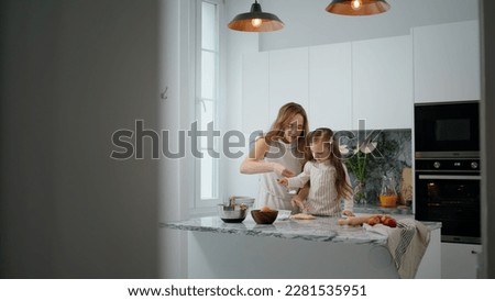 Involved mom and child kneading dough on table. Cute family preparing cookies pastry at contemporary home. Mother daughter cooking at kitchen together. Little girl helping woman in modern interior