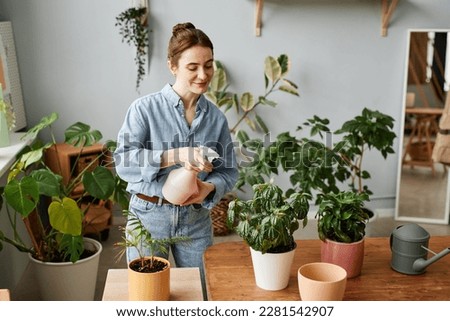 Portrait of smiling young woman watering plants indoors and caring for home greenery, copy space Royalty-Free Stock Photo #2281542907