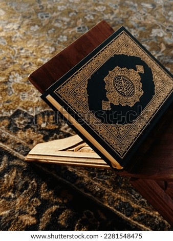 Al Quran Al Karim book on quran stand holder with sun ray light. Wrote on it "Al Quran Al Karim" in Arabic.