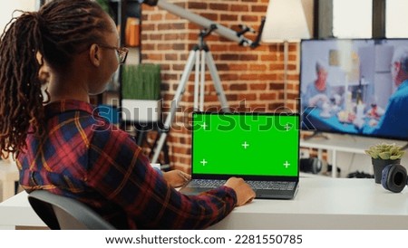 Female employee looking at greenscreen display on laptop, using isolated blank mock up template on wireless pc. Woman working with chroma key copy space background on home desk.