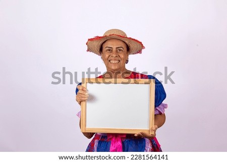 lovely elderly woman dressed for festa junina very happy posing for photo holding a white board
