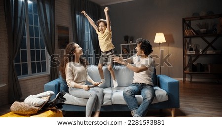 Excited naughty, noisy Asian child jumping around mom and dad on sofa, shouting, annoyed. hyperactive little son jumping on sofa and drawing attention. Royalty-Free Stock Photo #2281593881