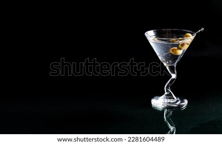 A classic vodka martini with a cocktail pick of green olives, against black.