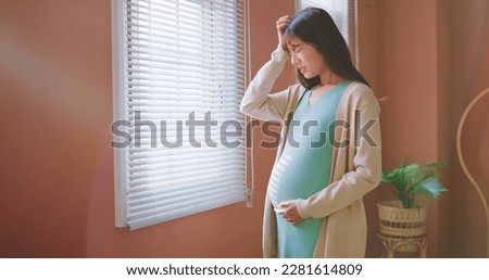 closeup asian pregnant woman standing by the window having headache and worried Royalty-Free Stock Photo #2281614809