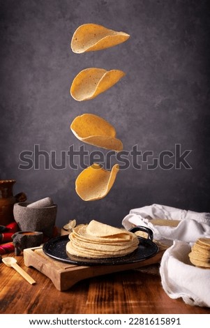 Corn tortillas falling on a Mexican griddle in a typical Mexican cuisine setting with a rustic wooden table and stone molcajetes. Royalty-Free Stock Photo #2281615891
