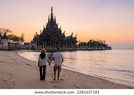 A couple of men and women visiting the Sanctuary of Truth, Pattaya, Thailand, wooden temple by the ocean during sunset on the beach of Pattaya. Temple of Truth in Thailand