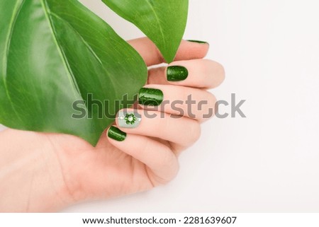 Female hand with vacation nail design. Glitter green nail polish manicure with rhinestone flower nail art. Female model hand with perfect green manicure on white background. Copy space. Place for text Royalty-Free Stock Photo #2281639607