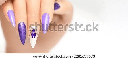 Female hand with stiletto nail design. Glitter purple nail polish manicure with purple rhinestones spider nail art. Female model hand on white background. Copy space