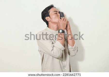 Portrait of Asian man communicating video call using smartphone. Indonesian man posing for a kiss while staring at the cellphone screen. Asian man in gray shirt on isolated white background Royalty-Free Stock Photo #2281662771