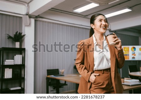 Portrait of a smart Asian young entrepreneur woman laughing and standing while holding a paper coffee cup in the office. Businesswoman wearing a blazer with a smile. Image with copy space.