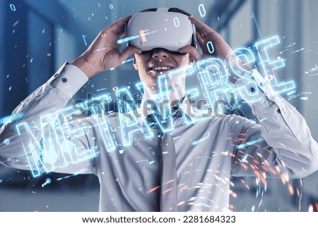 Cheerful young european businessman with VR glasses using glowing metaverse text hologram on blurry office interior tech background. Digital world and future concept. Double exposure