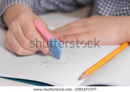 Boy erasing mistake in his notebook at white desk, closeup Royalty-Free Stock Photo #2281691597