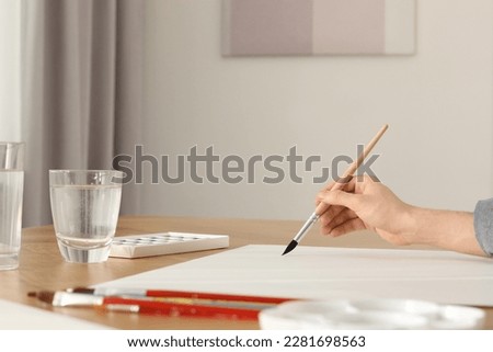 Woman with brush and paint at wooden table indoors, closeup. Watercolor artwork