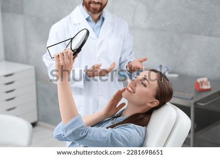 Young woman looking at her new dental implants in mirror indoors Royalty-Free Stock Photo #2281698651