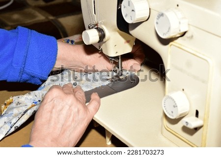 Hands of a seamstress at the moment when she sews the fabric with a sewing machine, side view.