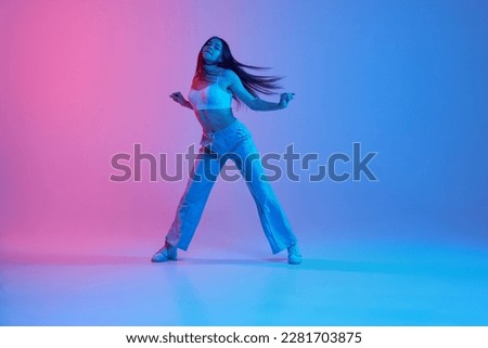 Young sportive girl dancing, training over gradient pink blue background in neon light. Hip-hop. Youth culture, style and fashion. Concept of dance, youth, hobby, dynamics, movement, action, ad