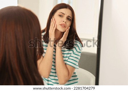Young woman looking in mirror and touching her face indoors. Hormonal disorders Royalty-Free Stock Photo #2281704279