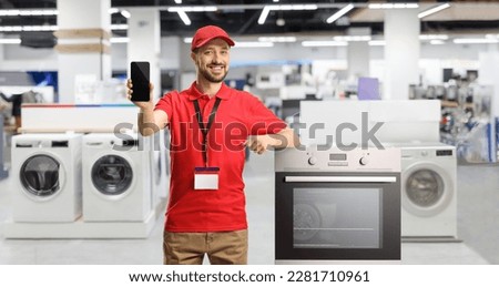 Male shop assistant with an oven smiling and showing a smartphone inside a store Royalty-Free Stock Photo #2281710961
