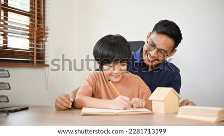 A caring and happy Asian father teaching his son to write the alphabet or draw a cute animal picture on a paper.