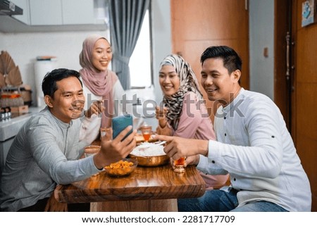 happy friends taking their picture together using a smartphone while having iftar dinner