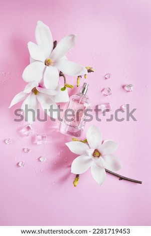 Open bottle of perfume with magnolia flowers, ice cubes, drops of water composition on the pink background. Fresh magnolia aroma. Idea of sweet pure smell of flowers for young girls. Place for text.  