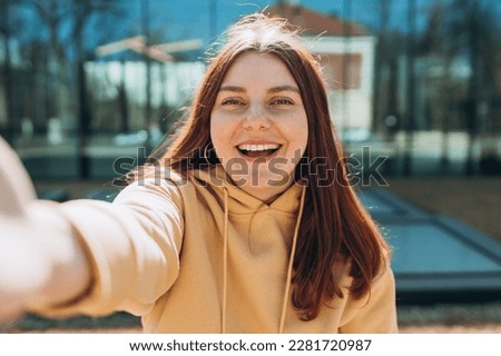 Young happy woman is making selfie on a camera on city street. Urban life concept. Girl talking on a video call with phone outdoor.