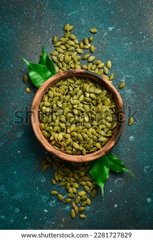 Peeled pumpkin seeds in a wooden bowl. On a dark textured background. Copy space.