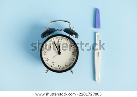 Still life with alarm clock and pregnancy test at work - the appearance of two stripes. Rapid diagnosis of pregnancy at home. Time of registration for pregnancy. Female health and fertility concept