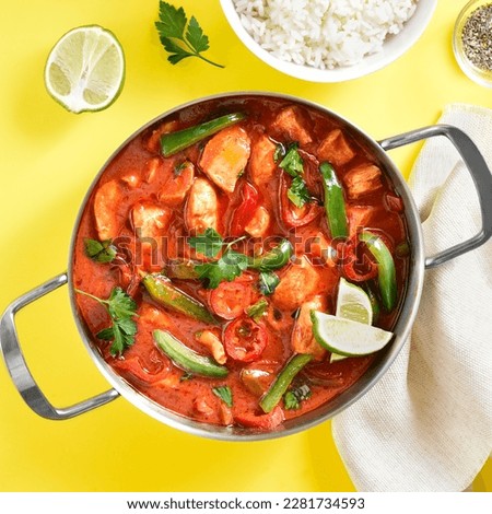 Thai style red chicken curry with vegetables in pan over yellow background. Top view, flat lay