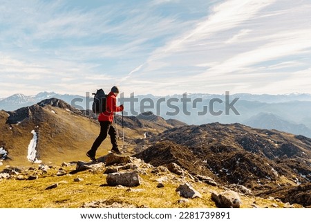 mountaineer man from behind with red clothes, backpack and trekking poles practicing high mountain hiking. outdoor sport and adventure.