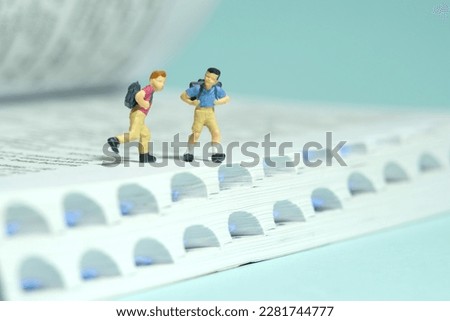 Miniature tiny people toys photography. Two boy with school backpack running above book. Isolated on blue background. Image photo