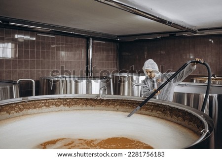 Portrait of male brewer standing by tank in brewery. Man examining the beer in processing section Royalty-Free Stock Photo #2281756183