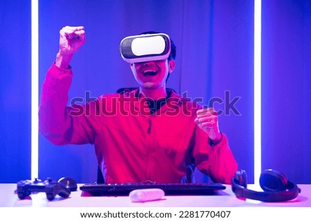 Asian man wearing VR glasses and playing games. While playing video games he is excited and surprised. by reaching out to touch something in the virtual world.