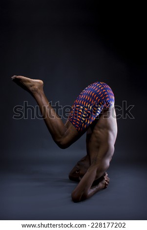 muscular black man doing upside down yoga on grey background